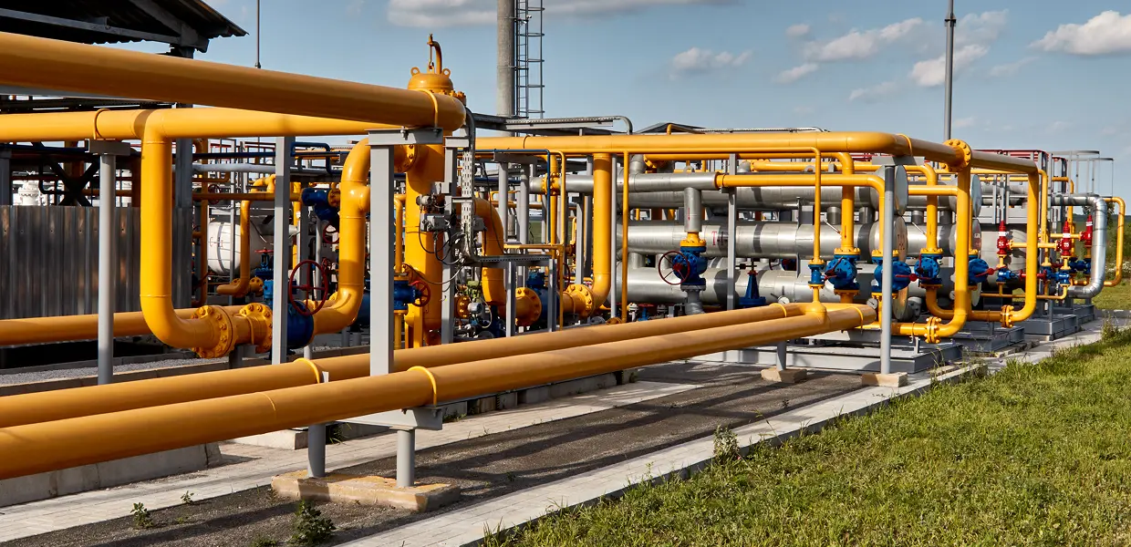 Industrial yellow pipelines at a gas processing facility under a clear sky.