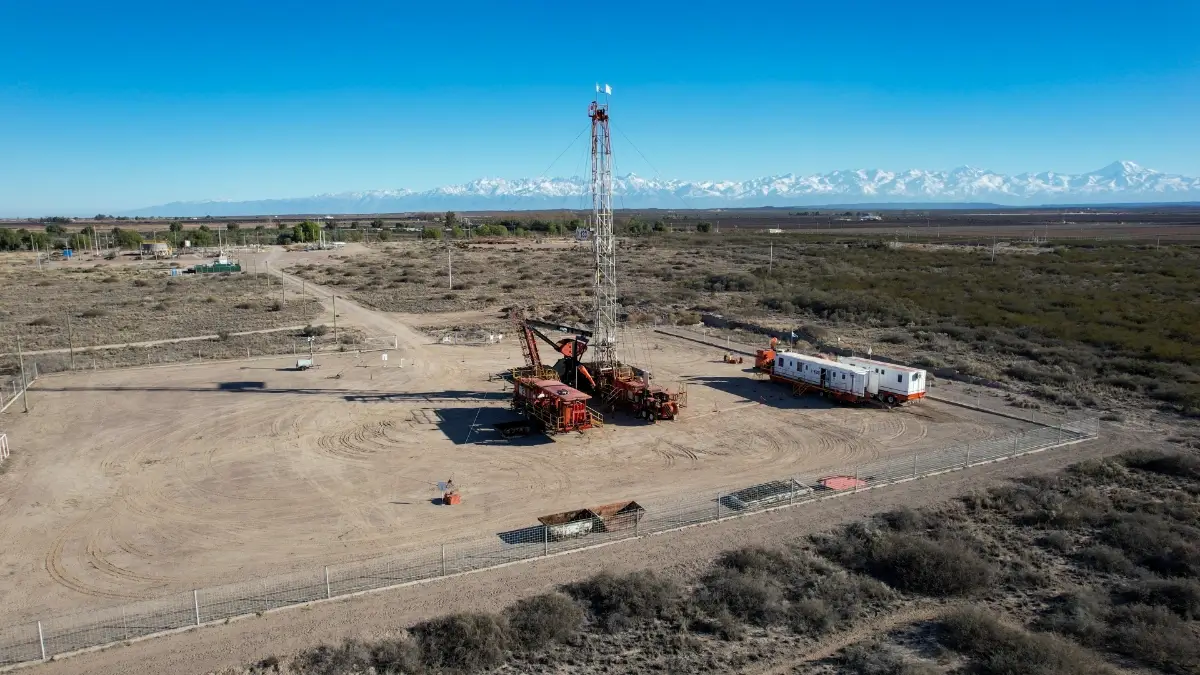 Oil drilling rig operating in a dry, flat landscape under a clear blue sky.