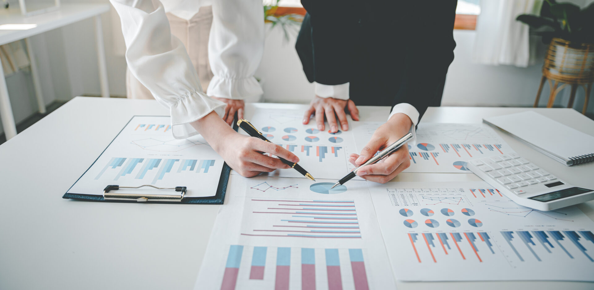 Two people analyzing business charts and graphs on paper with pens.