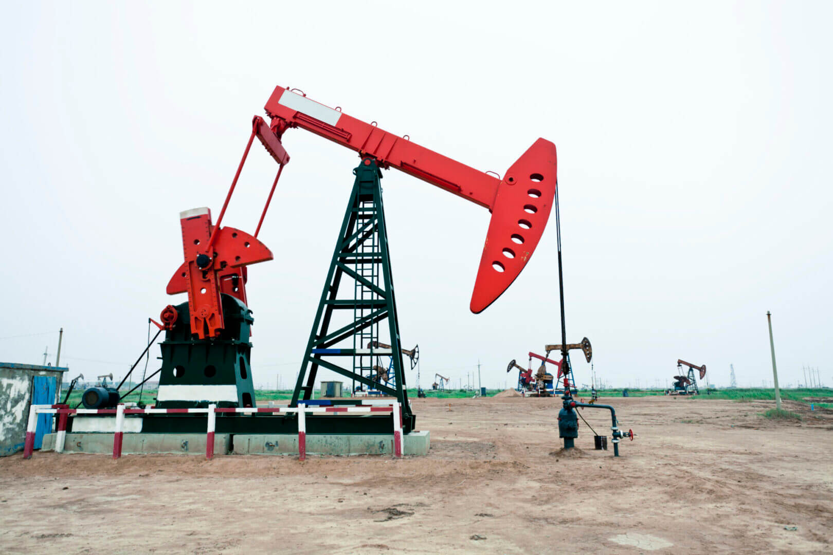 A red oil pumpjack extracting crude oil in a barren field.